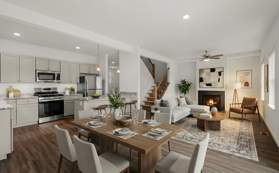 A wide-angle view of a modern open-concept living area featuring a kitchen with light grey cabinetry, granite countertops, and stainless steel appliances. The space flows into a dining area and a living room with a fireplace and large windows.