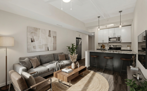 Photograph of a modern open-concept living room with grey sofa, armchairs, and a kitchen with white cabinets and dark island.