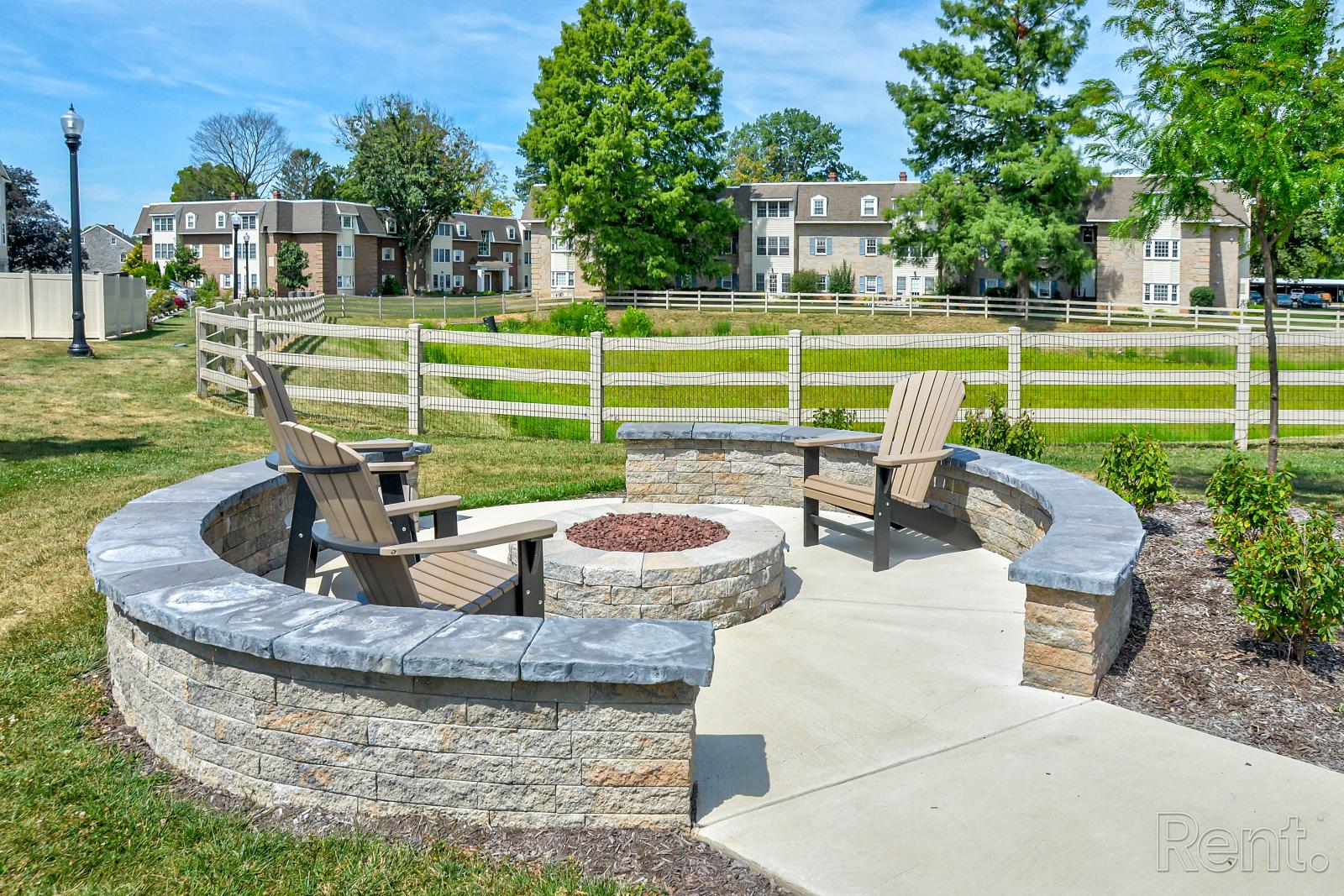 Stone fire pit with curved seating wall and Adirondack chairs in open grassy community space.
