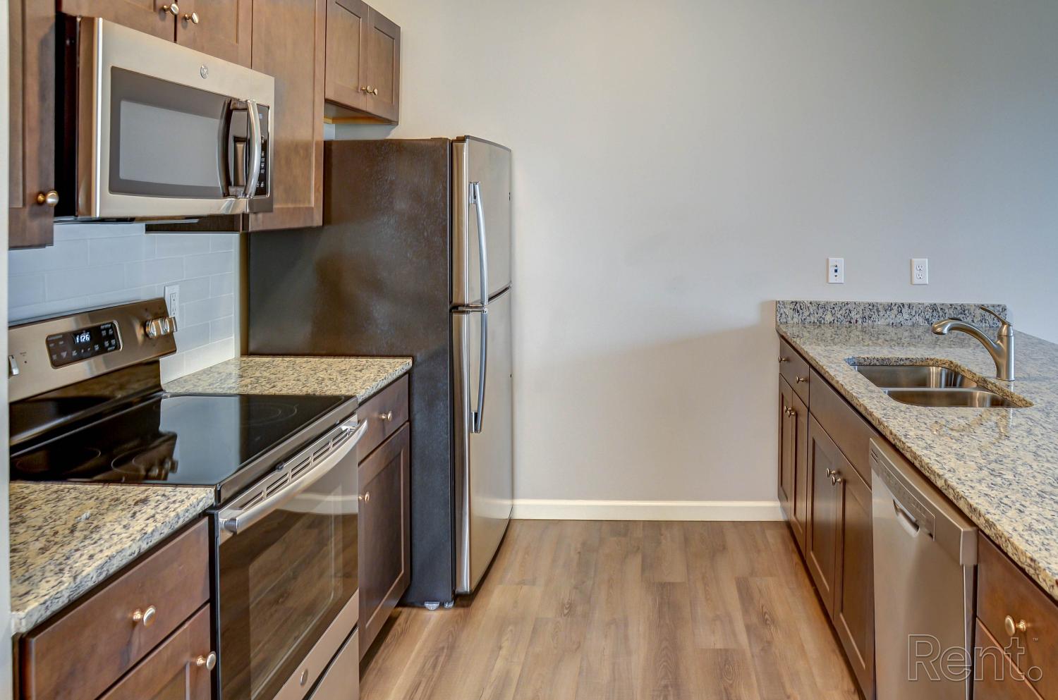 Modern kitchen with granite countertops, stainless steel appliances, dark wood cabinets, and wood-style flooring.