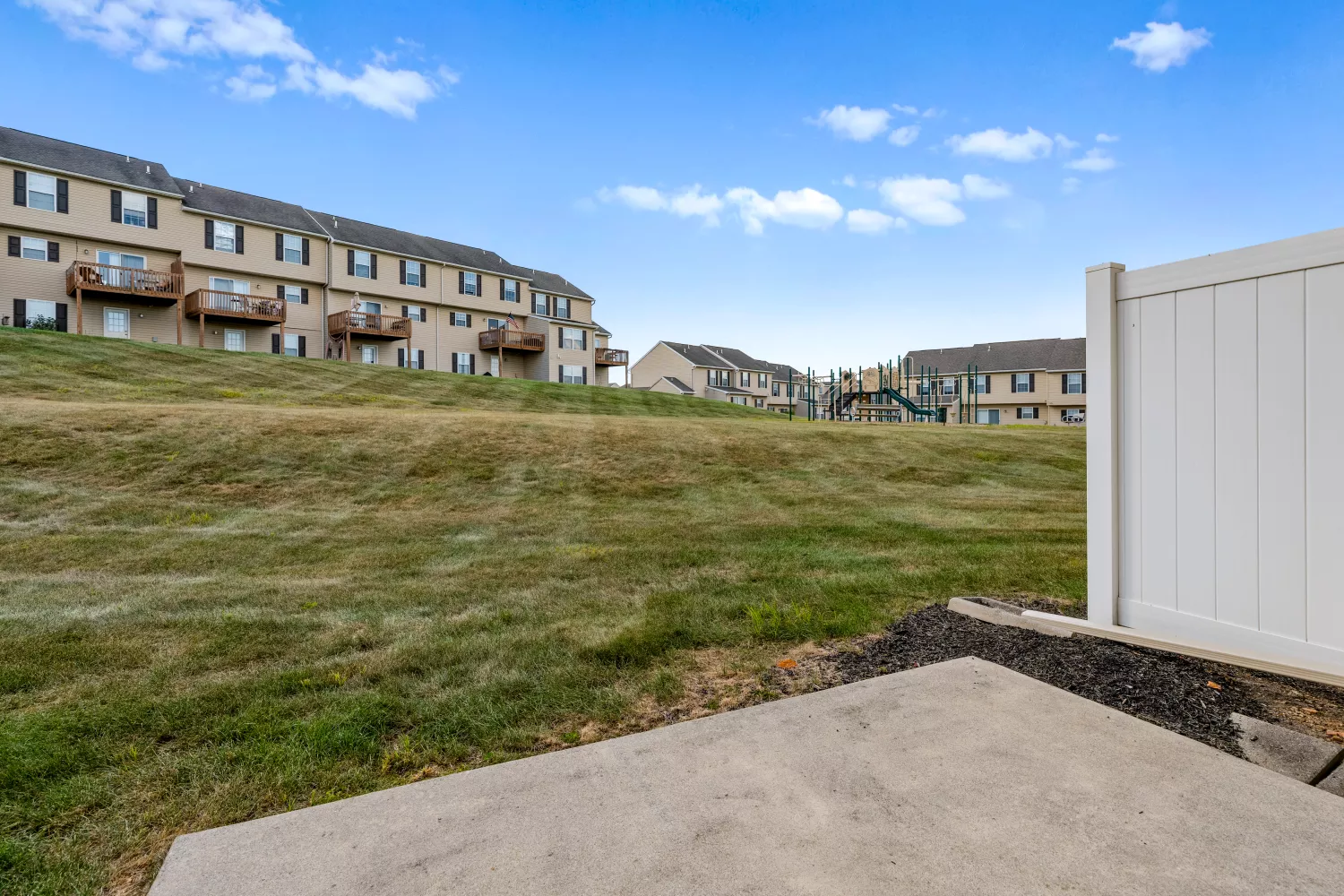 Outdoor green space at Windsor Commons Townhomes with wide lawns, balconies, and view of community playground