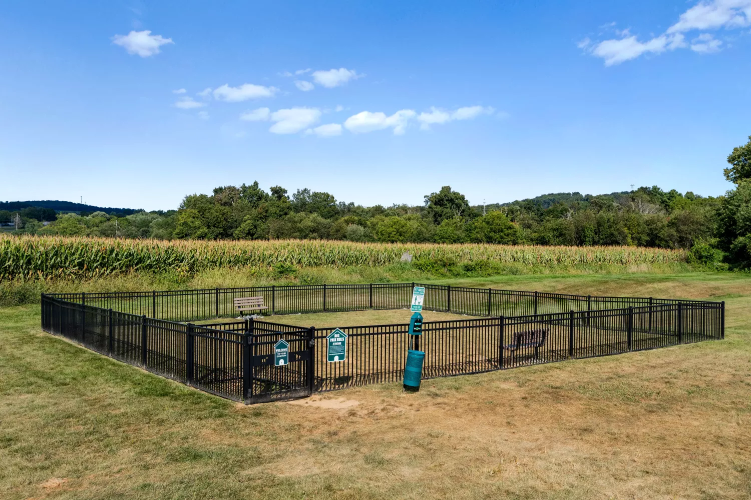 Fenced dog park at Windsor Commons Townhomes with benches, waste stations, and open green space for pet-friendly living.
