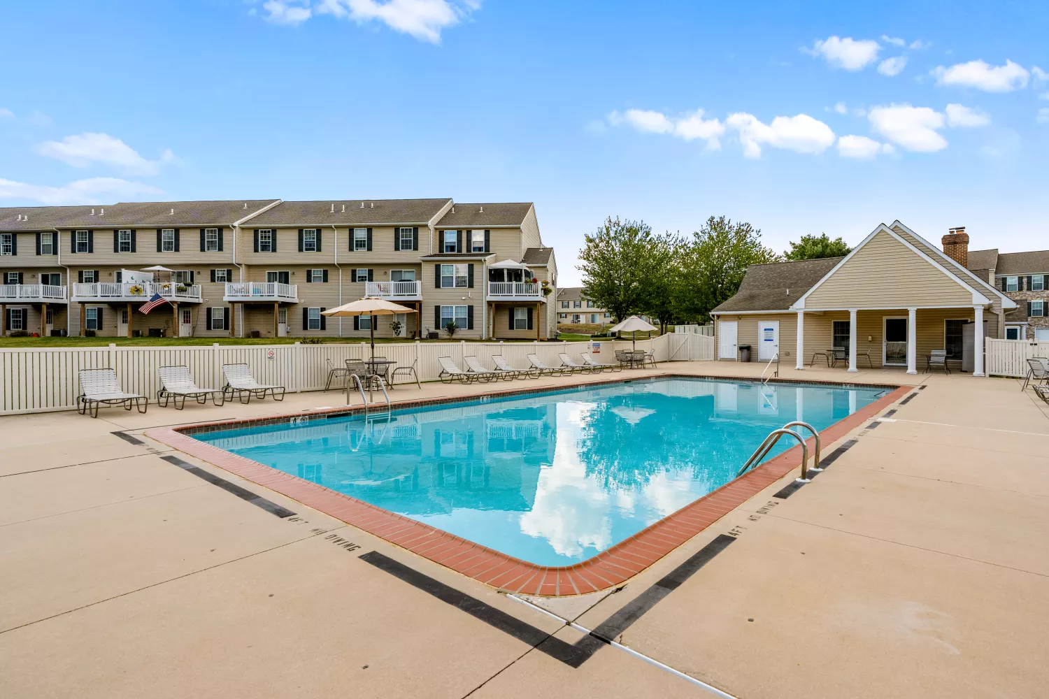 Outdoor swimming pool at Windsor Commons Townhomes with lounge chairs, umbrellas, and fenced patio area.