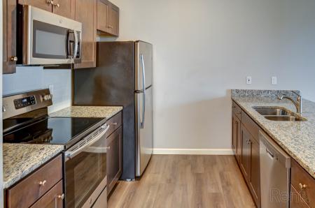 Modern kitchen with granite countertops, stainless steel appliances, dark wood cabinets, and wood-style flooring.