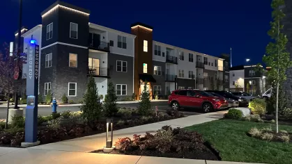 Exterior view of The Foundry apartment building at night with illuminated emergency call box, modern landscaping, and parked vehicles.