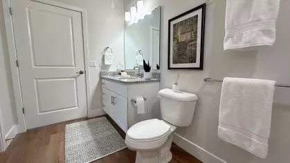 Stylish bathroom with granite countertop vanity, framed mirror, towel bars with white linens, and decorative wall art above the toilet.