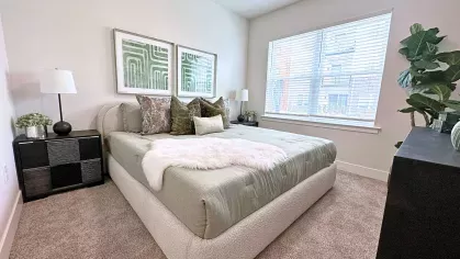Furnished bedroom with carpeted floors, neutral décor, large window with blinds, and ample natural light highlighting the cozy layout.
