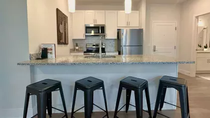 Kitchen with granite island featuring bar seating for four, pendant lighting, and open access to living space and entryway.
