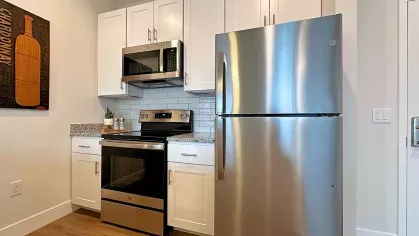 Compact kitchen featuring stainless steel appliances, granite countertops, white shaker-style cabinets, and subway tile backsplash.