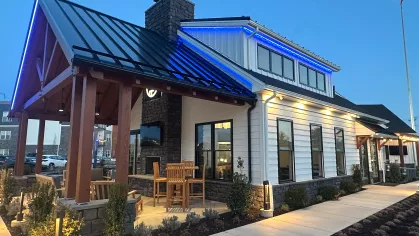 Interior of The Foundry clubhouse featuring a stone fireplace, modern seating with leather couches and lounge chairs, and tall windows allowing natural light.