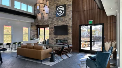 Inside view of The Foundry's social lounge with high ceilings, contemporary lighting fixtures, a TV-mounted stone fireplace, and stylish seating options.