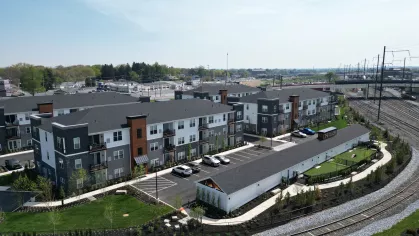 Daytime aerial photo of The Foundry apartment community showing multiple modern buildings, walking paths, and well-maintained green spaces along a railroad track.