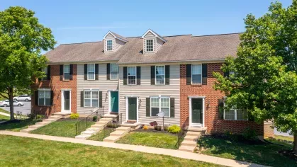 Sunny exterior view of Mill Creek Manor townhomes with brick and siding facades, individual entrances, and landscaped walkways.