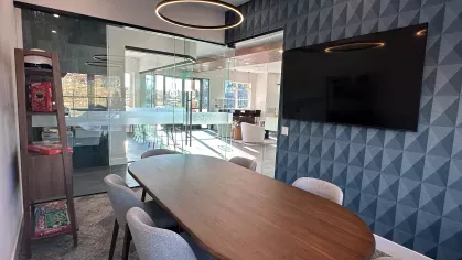 Work-from-home conference space featuring a long table with upholstered chairs, mounted TV, and shelving stocked with board games.