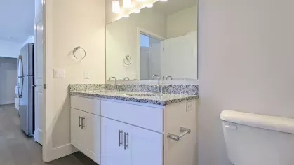 Modern bathroom with a granite countertop vanity, single sink, and wall-mounted mirror, featuring bright overhead lighting and sleek cabinetry.