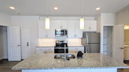 Modern kitchen with stainless steel appliances, white cabinetry, granite countertops, and subway tile backsplash, centered around a large island.