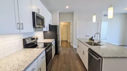 Side view of kitchen highlighting sleek appliances, ample cabinetry, and long granite island with pendant lighting and open layout.