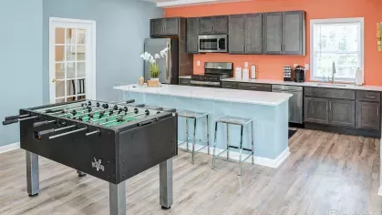 Modern clubhouse kitchen with stainless steel appliances, breakfast bar seating, and vibrant orange accent wall