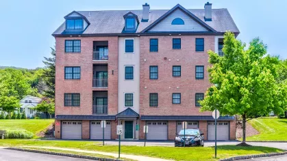 Multi-story apartment building with garage-level entry, private balconies, and tree-lined streets in a suburban setting.