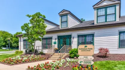 Bethlehem Fields leasing office with white siding, green trim, colorful flower beds, and clear directional signage near the entrance.