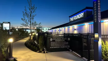 Nighttime view of The Foundry’s fenced dog park entrance, lit pathway, and signage with emergency contact information and pet rules.