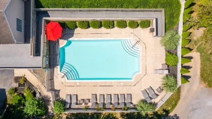 Aerial view of the Mill Creek Manor outdoor pool area with lounge chairs, red umbrella, and privacy landscaping