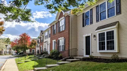 Tree-lined street view of Mill Creek Manor townhomes featuring brick and vinyl siding with front steps and sidewalks