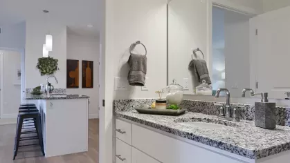 Bathroom with granite countertop vanity and decorative accents, looking into the open kitchen with bar stools and pendant lighting.