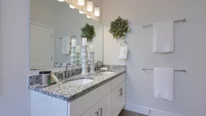 Elegant bathroom with dual sinks, granite countertops, decorative candle holders, and three-light vanity fixture above a large mirror.