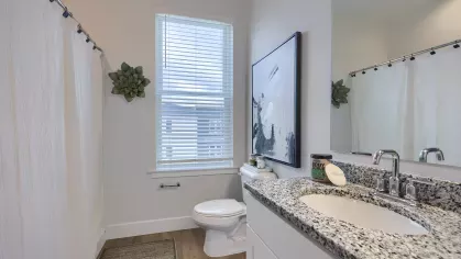 Bathroom featuring granite vanity, abstract framed art, window with blinds, and white shower curtain over a full bathtub.