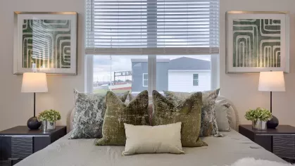 Inviting bedroom with plush bedding, decorative throw pillows, framed geometric wall art, and a large window letting in natural light.
