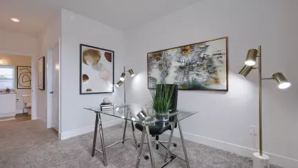Contemporary home office with a glass desk, leather chair, abstract wall art, and view into adjacent bathroom at The Forge apartment community