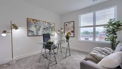 Sunlit office space with large window, modern desk setup, cozy gray couch, and decorative plants at The Forge apartments.