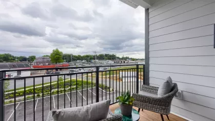 Private balcony with two wicker chairs, a small accent table, and a view of the neighborhood and parking lot at The Forge apartments.