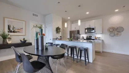 Spacious kitchen with white cabinets, granite countertops, stainless steel appliances, and adjacent dining area with modern furnishings at The Forge apartments.