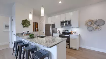 Sleek kitchen with granite countertops, stainless steel appliances, white cabinetry, and pendant lighting above a breakfast bar with black stools.