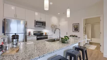 Contemporary kitchen with granite counters and stainless steel appliances, opening to a hallway with a view of a modern bathroom.