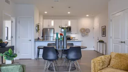 Dining area with modern black chairs and table set in front of a granite kitchen island and stainless steel appliances.