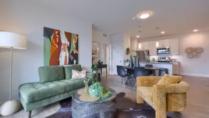 Living room featuring a green velvet sofa, bold abstract wall art, gold accent chair, and a cowhide rug over light hardwood floors.