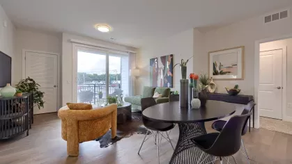 Inviting open-concept layout with a green sofa, golden armchair, round coffee table, and view into the kitchen and dining area.