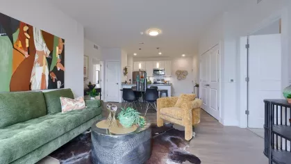 Inviting open-concept layout with a green sofa, golden armchair, round coffee table, and view into the kitchen and dining area.