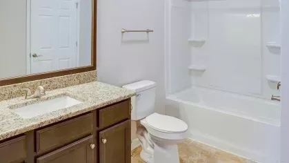 Renovated bathroom with granite countertop, dark wood vanity, full-size mirror, toilet, and white shower-tub combo.