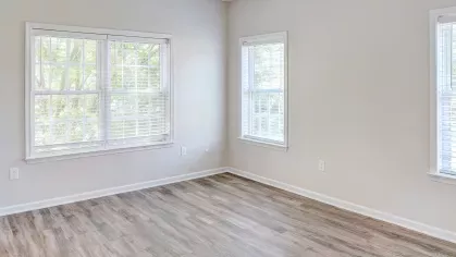 Spacious bedroom with light walls, large corner windows, and wood-style vinyl flooring in a renovated apartment unit.
