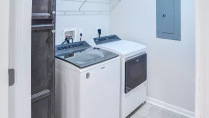 Modern laundry room with top-load Whirlpool washer and dryer, overhead wire shelving, and built-in storage cabinet.