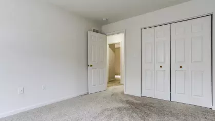 Spacious bedroom featuring a wide double-door closet and an open doorway leading to the hallway, complete with plush carpeting and light-colored walls.