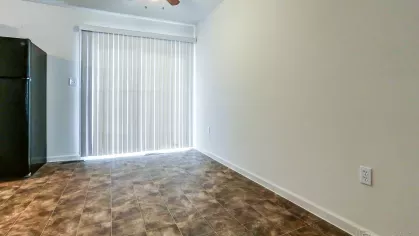 Dining space with vinyl tile flooring, a ceiling fan with light, and vertical blinds covering a sliding glass door for natural light and backyard access.