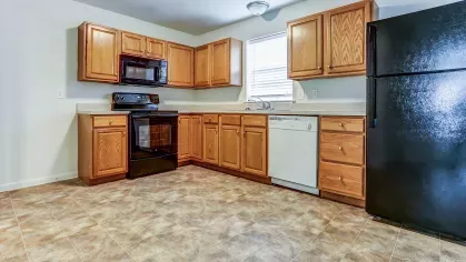 Well-equipped kitchen with black and white appliances, natural wood cabinetry, and ample counter space, accented by a large tile-patterned floor.