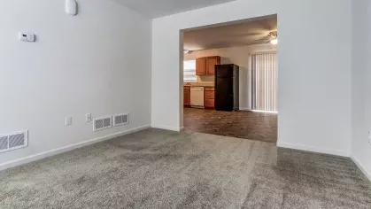 View from the living room into the open kitchen and dining area, featuring carpeted and tiled floors and modern light fixtures.