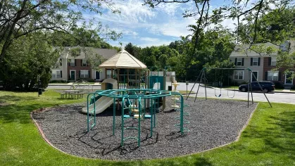 Colorful playground with slide, swings, climbing equipment, and picnic table surrounded by trees and townhomes, perfect for family fun at Mill Creek Manor.
