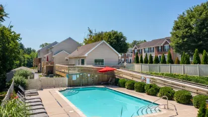 Elevated view of pool area, clubhouse, and surrounding townhomes with manicured shrubs, fencing, and red umbrella for shaded seating.